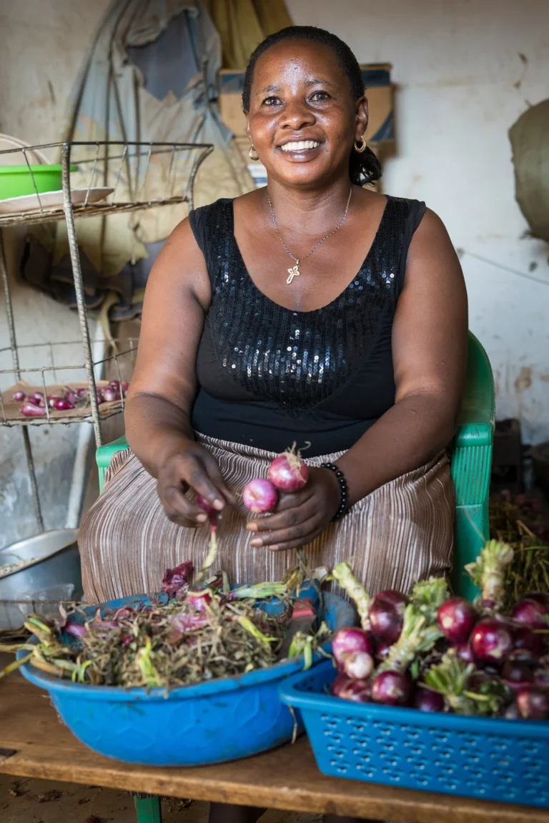 A smiling woman sorting onions and vegetables into baskets at her produce business