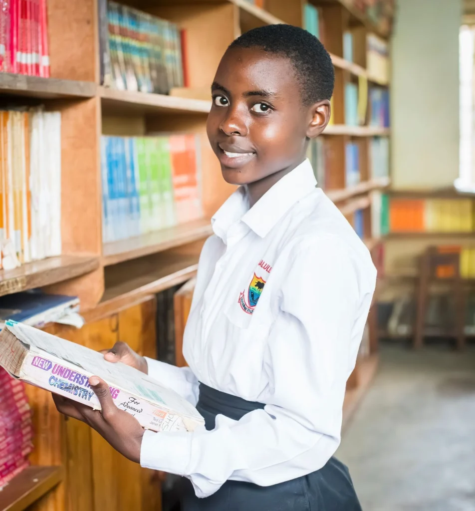 A student in school uniform reading a book beside library shelves
