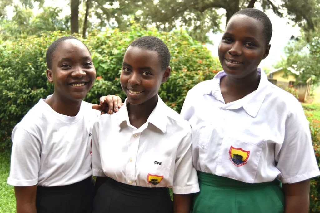 Three students in school uniform standing arm in arm and smiling