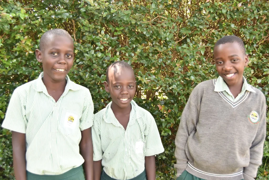 Three boys in school uniform standing together in front of a hedge