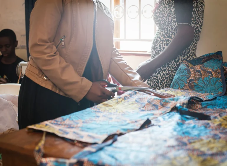 Hands measuring and cutting colourful African print fabric in a tailoring class